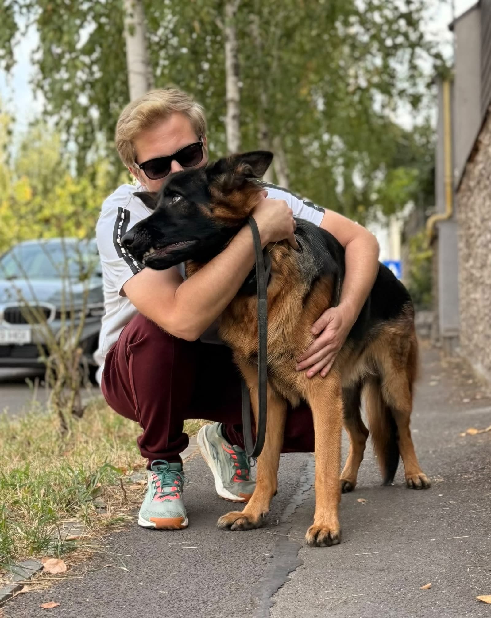 Adi, pe vine, îmbrățișând un ciobănesc german pe trotuar